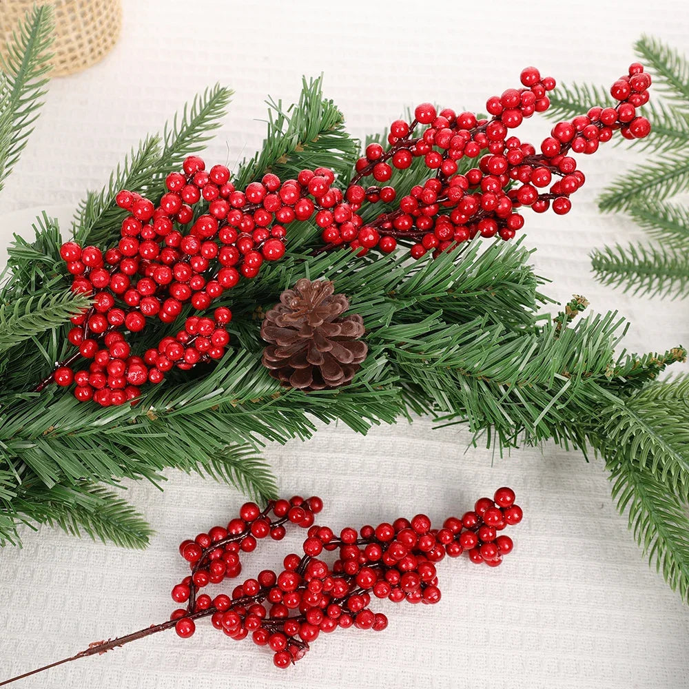 A branch of green pine needles decorated with clusters of bright red artificial holly berries for Christmas decor