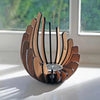 A wooden lotus candle holder decoration with multiple curved slats and a central holder, placed on a windowsill.