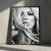 A black and white portrait of a woman with long blonde hair holding a cigarette, framed in a dark border.