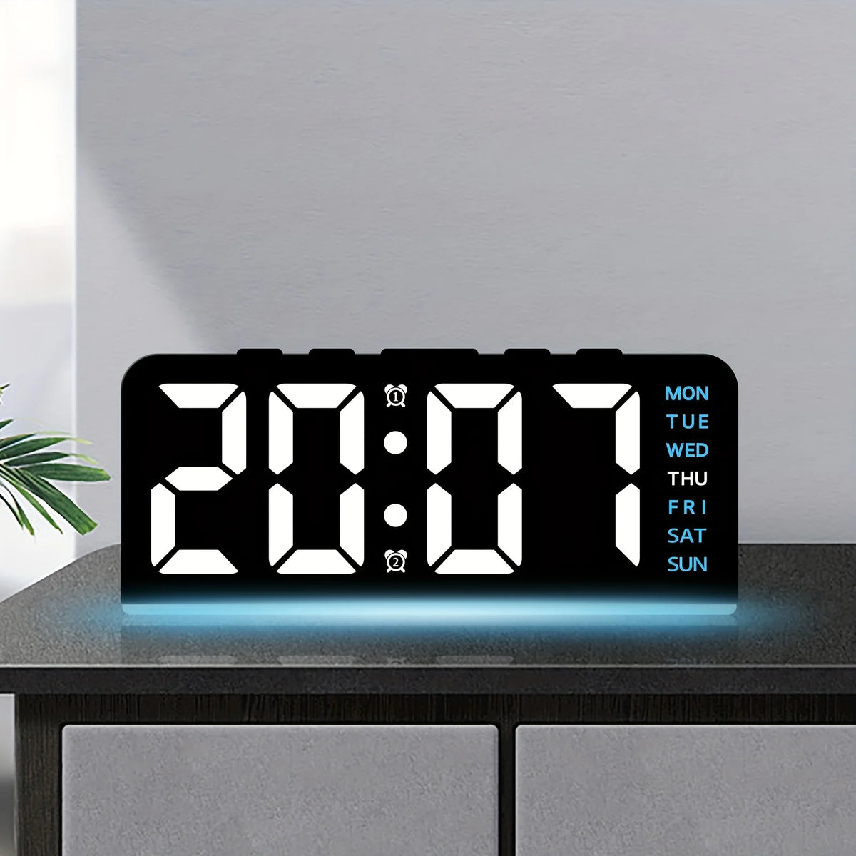 Reloj de alarma digital LED negro mostrando 20:07 con un brillo azul sobre una superficie oscura.