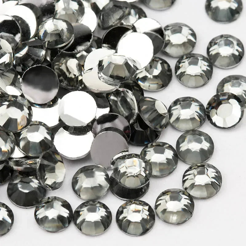 A close-up view of small, round flatback resin rhinestones in silver and clear tones scattered on a white background.