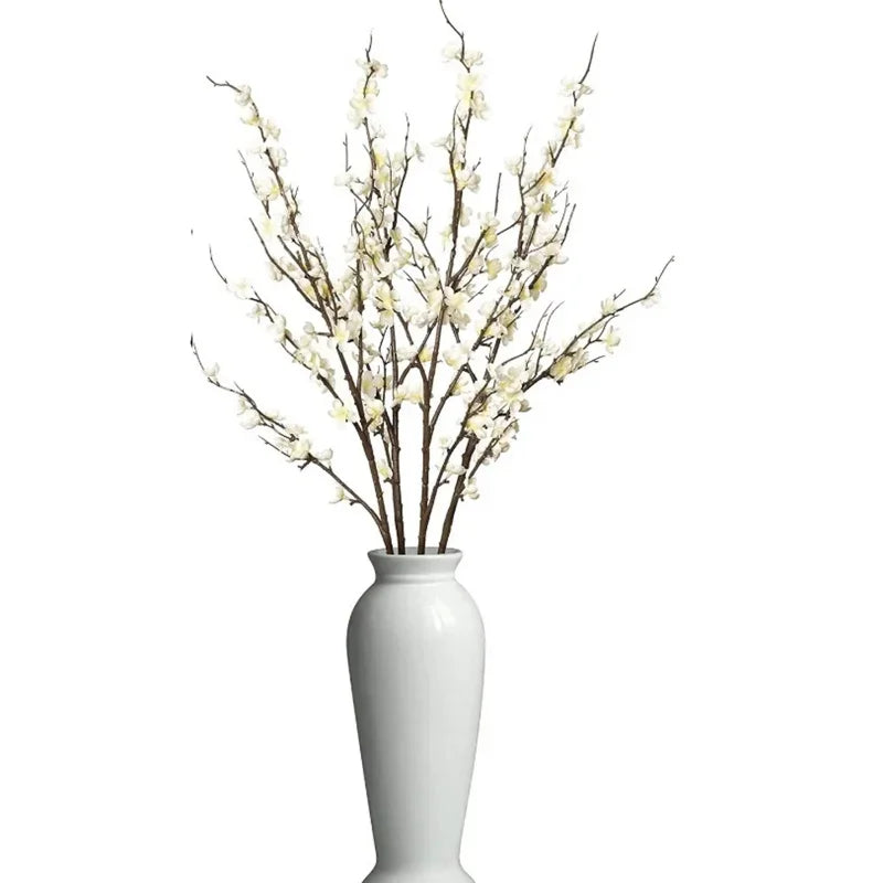 A branch of real touch faux plum blossoms with stems in a white vase.