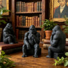 A dark, 3D-printed gorilla figurine sitting on a wooden surface surrounded by books and plants.