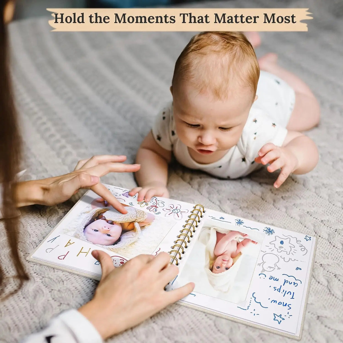 A close-up of a baby and an adult holding open a linen cover photo scrapbook album on a textured blanket.
