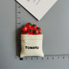 A small cream-colored pouch filled with red cherry tomatoes, labeled TOMATO, placed next to a ruler.