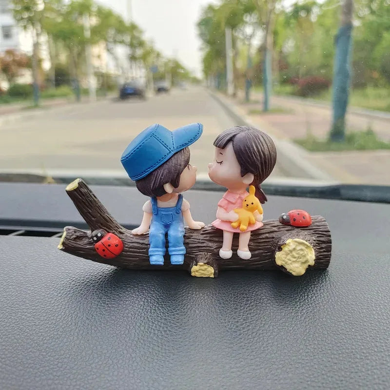 A set of two cute figures, a boy and a girl, dressed in blue and pink, sitting on a wooden branch with insects.