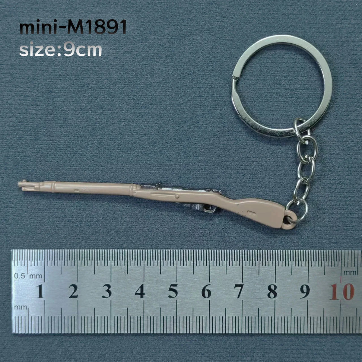 A miniature alloy gun model keychain with a light beige finish is shown next to a ruler for scale.
