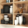 A set of stackable reusable plastic tableware in various shades of gray and white stored on wooden shelves.