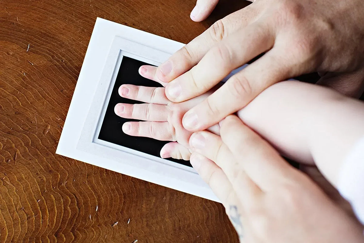 Hands print on a white frame showing baby handprint and footprint ink pad kit