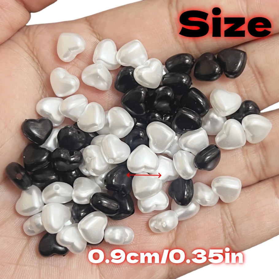 A pile of heart-shaped acrylic beads in black and white colors is shown on a hand.