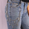 Close-up of light blue denim jeans featuring a layered silver charm belt with cross pendants and a large ring.