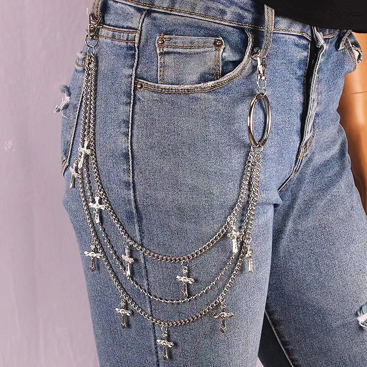 Close-up of light blue denim jeans featuring a layered silver charm belt with cross pendants and a large ring.