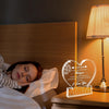 A clear acrylic heart plaque with a floral design is displayed on a bedside table next to a lamp.