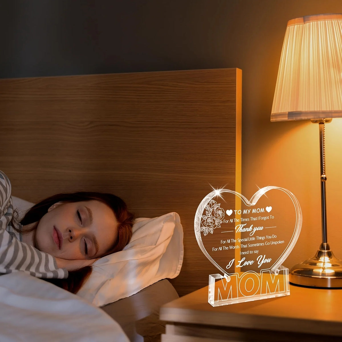 A clear acrylic heart plaque with a floral design is displayed on a bedside table next to a lamp.