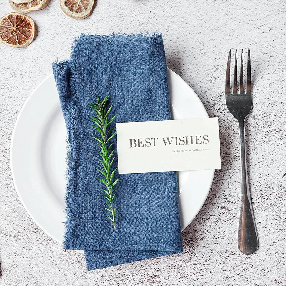 A set of ten handcrafted fringed cotton napkins placed on a white plate with a fork and a greeting card.
