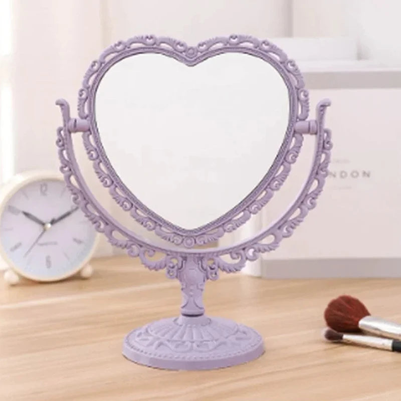 Espejo de maquillaje en forma de corazón morado con marco ornamentado sobre una superficie de madera.