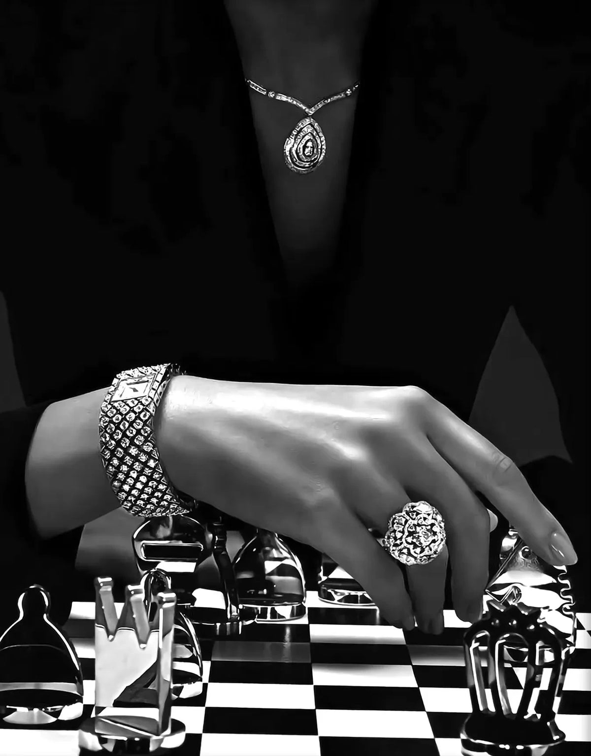 A hand wearing a diamond bracelet is resting on a black and white checkered surface with various glass objects.