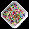 A small white dish filled with multicolored flatback resin rhinestones in various shades of pink, green, and blue.