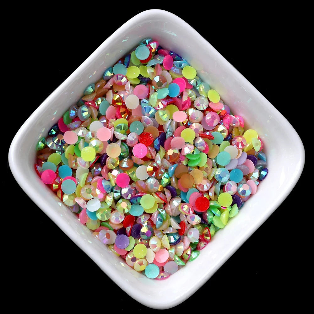 A small white dish filled with multicolored flatback resin rhinestones in various shades of pink, green, and blue.