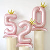 Pink foil number balloons 52 with gold crowns displayed on white columns