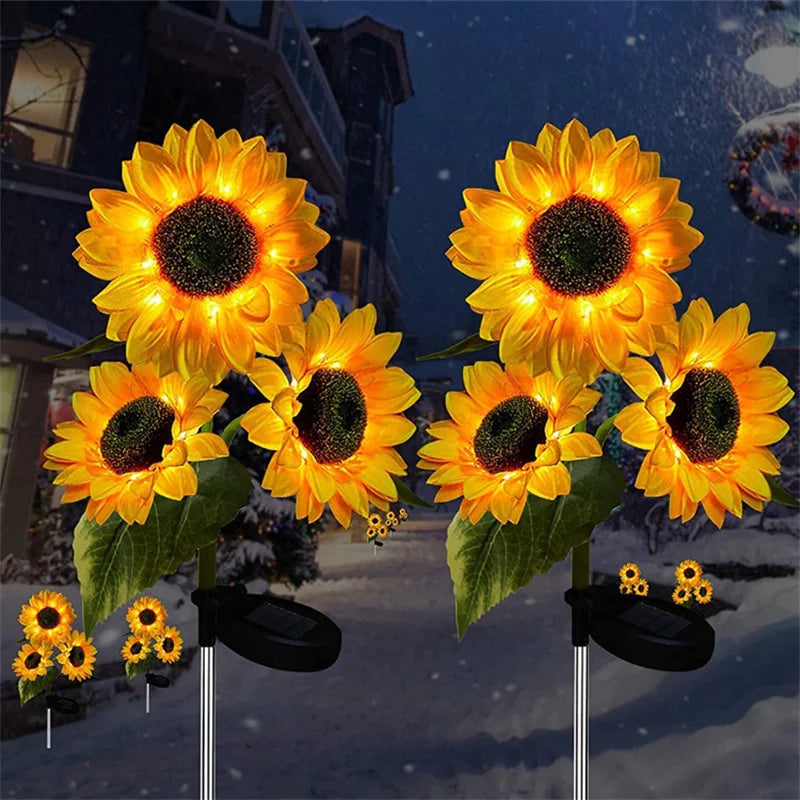 A cluster of bright yellow solar sunflower LED garden lights with black centers and green leaves against a snowy night backgr