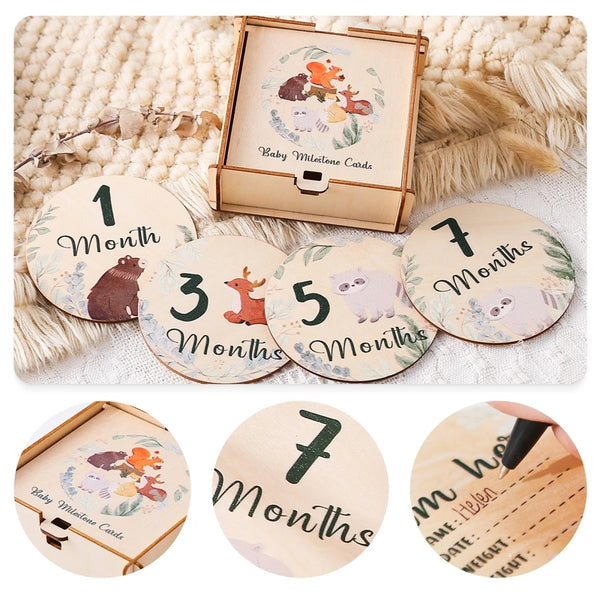 A set of wooden baby milestone cards showing months 1 through 7 with animals, displayed alongside a wooden keepsake box.