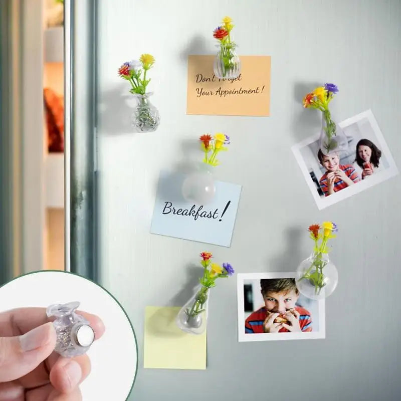 A hand holds a clear glass flower vase with yellow and red flowers, used for fridge decor.
