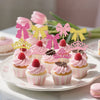 A display of pink and gold elegant crown and bow cupcake toppers on a white platter.