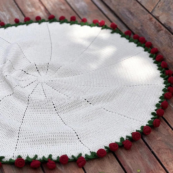 Bouquet de roses fait main, couverture tricotée crème avec bordure florale rouge sur une surface en bois.