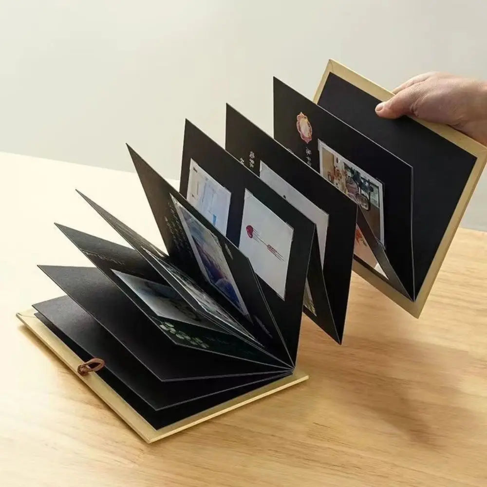 A hand holds open a black memory scrapbook album displaying photos and mementos.