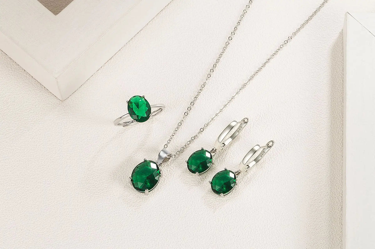 طقم مجوهرات فضة ستيرلينغ مع أحجار زمرد خضراء وسلاسل فضية على خلفية بيضاء.