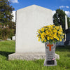 A white granite tombstone with an inscription and a vase of yellow flowers placed in front of it.