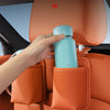 A hand places a light blue water bottle into a storage slot on an orange car seat back organizer.