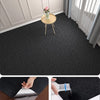 A close-up view of a black self-adhesive runner rug being applied to a wooden floor.
