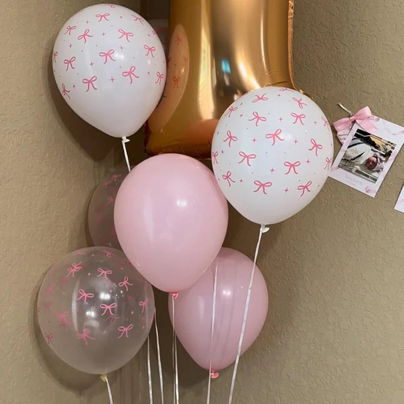 A cluster of pastel pink and white balloons tied with pink bows against a neutral background.