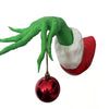 Green monster hand with long fingers holding a red Christmas ornament