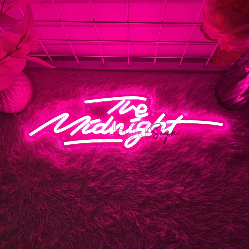 A neon sign spelling out The Midnight is displayed on a textured pink wall.