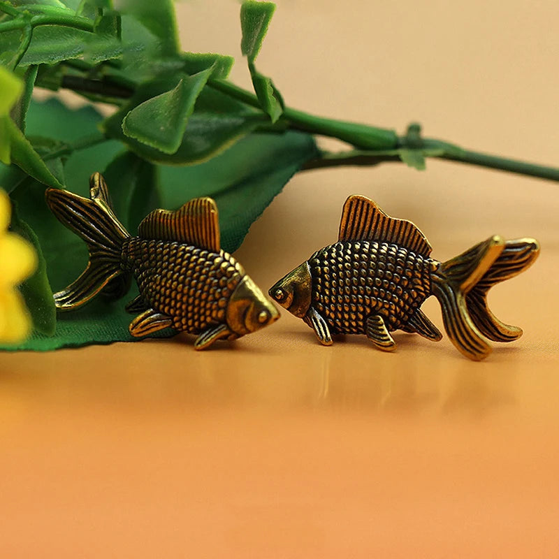 A pair of retro brass goldfish statues resting on a smooth surface with green foliage in the background.