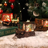 A miniature brass train music box with LED lights and a crystal ball sits on snow in front of a decorated Christmas tree.