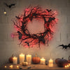 A dark branch bat wreath made of artificial black branches and pink lights hangs on a white brick wall.