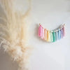 Handmade boho rainbow tassel garland featuring colorful threads and wooden beads hanging against a white background.