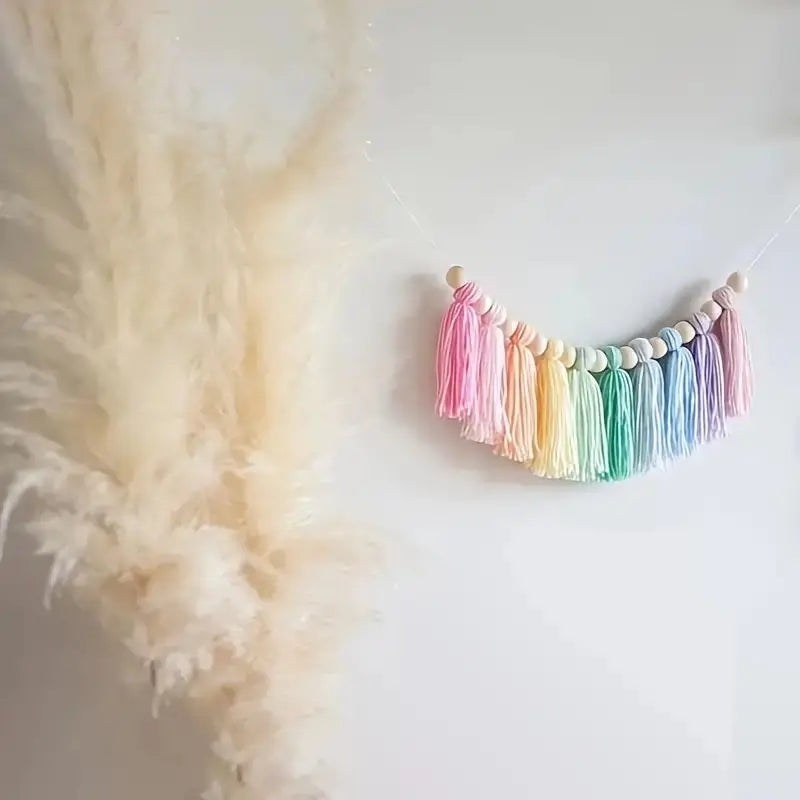 Handmade boho rainbow tassel garland featuring colorful threads and wooden beads hanging against a white background.