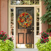 A dark brown door decorated with a vibrant autumn wreath of red, orange, and yellow artificial flowers.