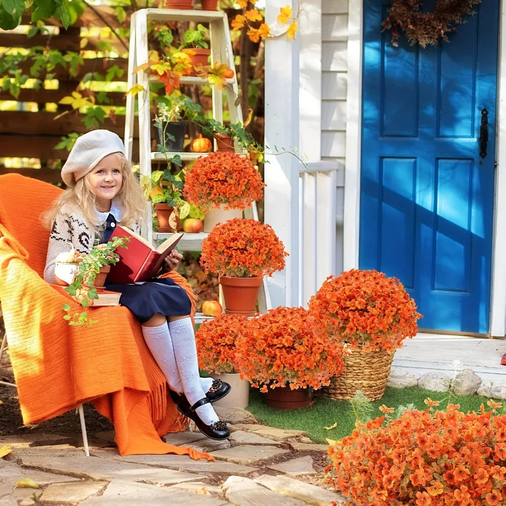 A young girl sits outdoors in an orange chair surrounded by potted orange flowers and a blue door.