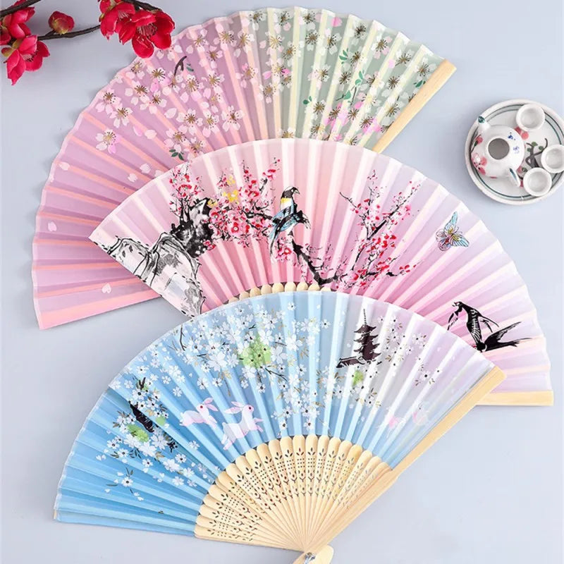 Three folding silk hand fans in pink, green, and blue featuring floral and bird designs.