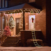 A festive outdoor display featuring a Santa Claus climbing ladder decorated with Christmas lights and draped garlands.