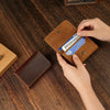 A hand is opening a brown leather card holder to reveal a blue credit card and cable organizer inside.