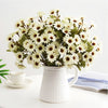 A bouquet of white and green artificial gerbera daisy flowers in a white pitcher on a white table.