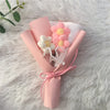 A pink and white handcrafted crochet sunflower bouquet tied with pink ribbon on a fluffy white surface.