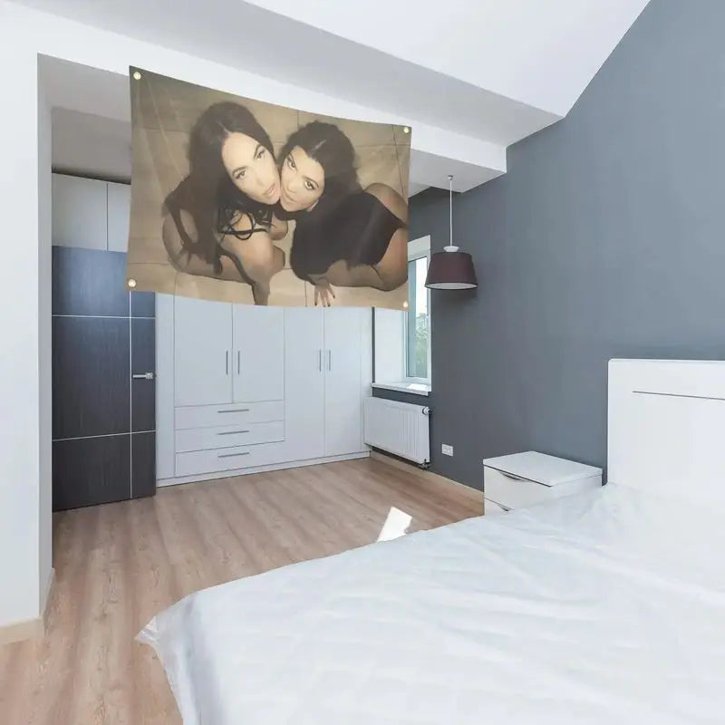 A tapestry featuring a close-up portrait of two women in black and gold tones hanging on a gray wall above a wooden floor.